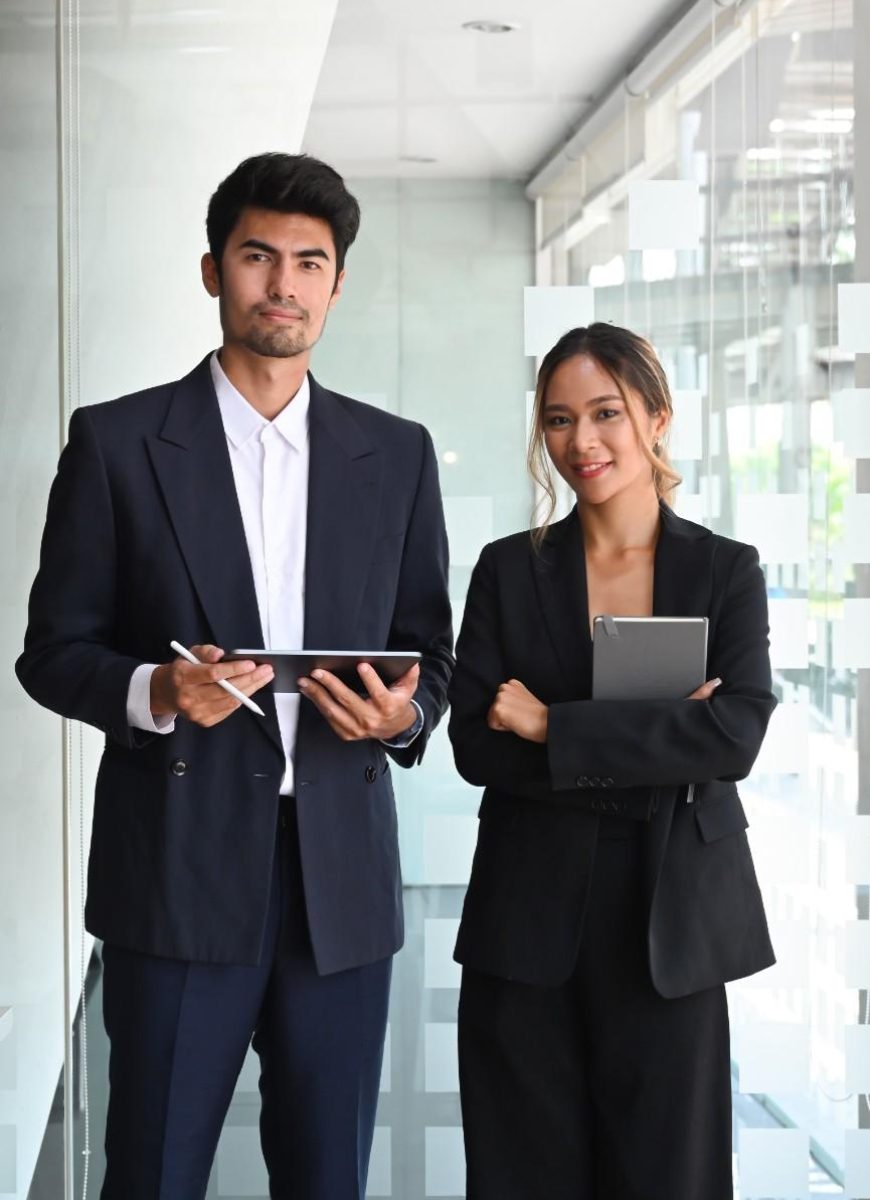 two-professional-businesspeople-holding-digital-tablet-looking-camera-while-standing-office-lobby-hall (1)
